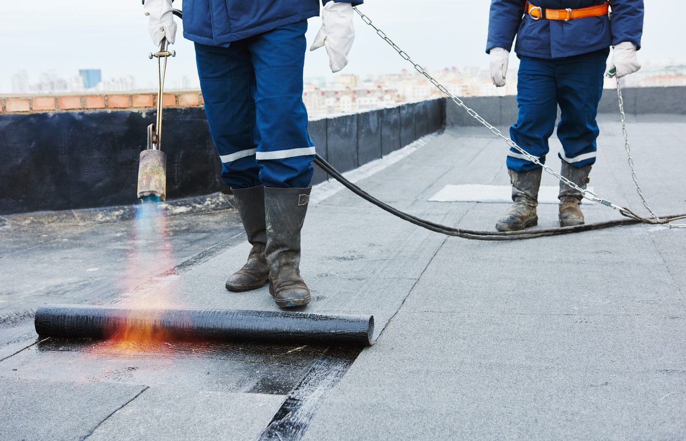 Roofer heat-welding torch-on felt during a flat roof installation